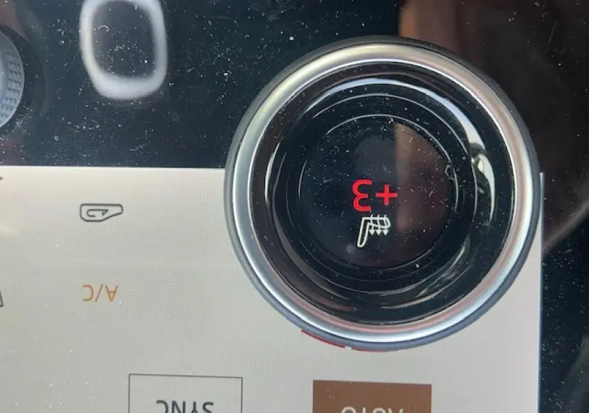 Gros plan sur le bouton de réglage de la température du siège chauffant dans le tableau de bord du Range Rover Evoque gris foncé.