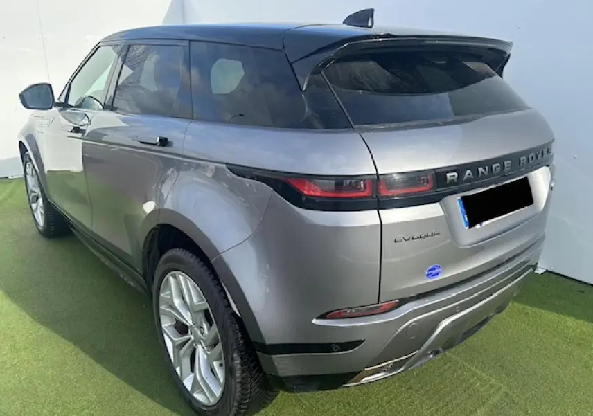 Vue 3/4 arrière droite d'un Range Rover Evoque gris foncé avec toit noir et jantes 20 pouces sur sol vert.