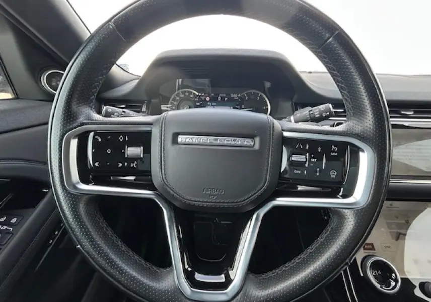 Volant cuir noir avec commandes intégrées et logo Range Rover, tableau de bord et écran tactile partiel visibles.