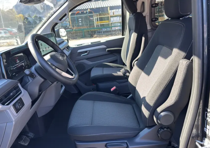 Vue intérieure côté conducteur du Volkswagen Transporter TDI 170 DSG ProCab 2026 avec sièges tissu gris et tableau de bord digital.