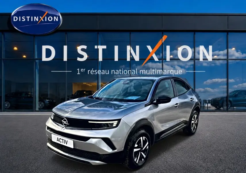 Opel Mokka gris en 3/4 avant droit, avec jantes noires et calandre noire brillante devant showroom Distinxion.