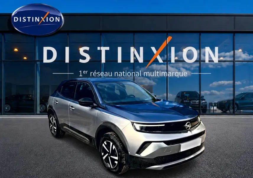 Opel Mokka gris 3/4 avant droit, avec jantes noires et toit noir, devant vitrine Distinxion.
