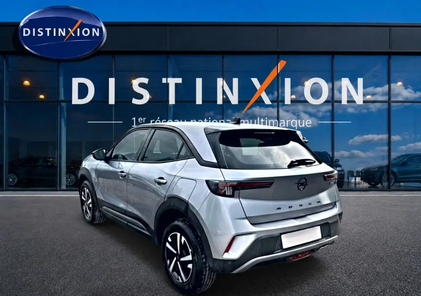 Vue 3/4 arrière droite d'un Opel Mokka gris 2025 devant une vitrine Distinxion, avec feux arrière LED et jantes noires.