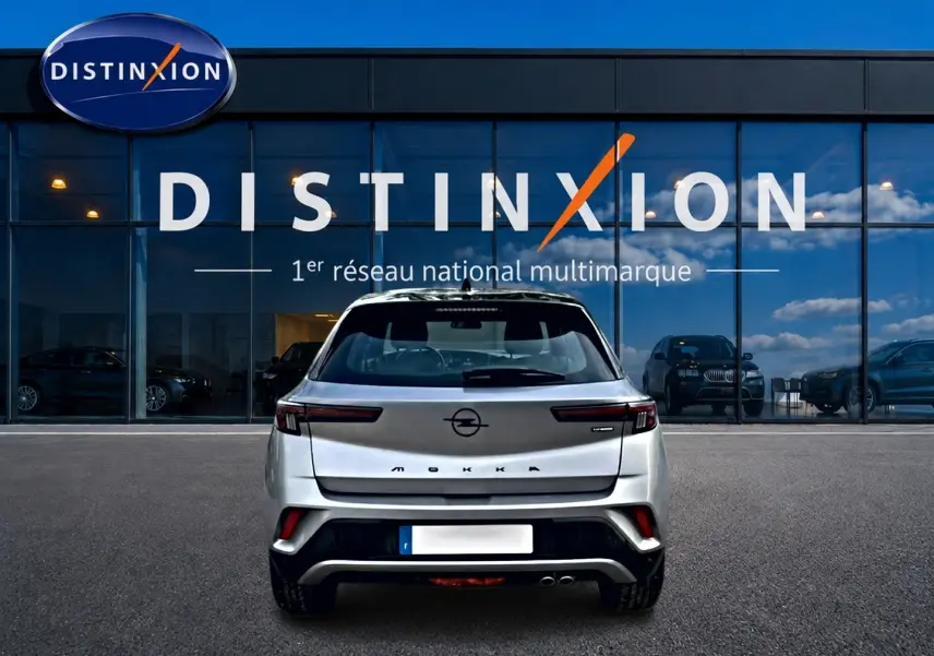 Vue arrière d'un Opel Mokka gris 2025 garé devant une vitrine avec logo Distinxion en arrière-plan.