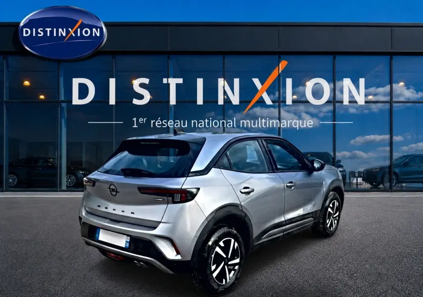 Vue 3/4 arrière droite d'un Opel Mokka gris 2025 devant une vitrine Distinxion, avec feux arrière LED et jantes stylisées.