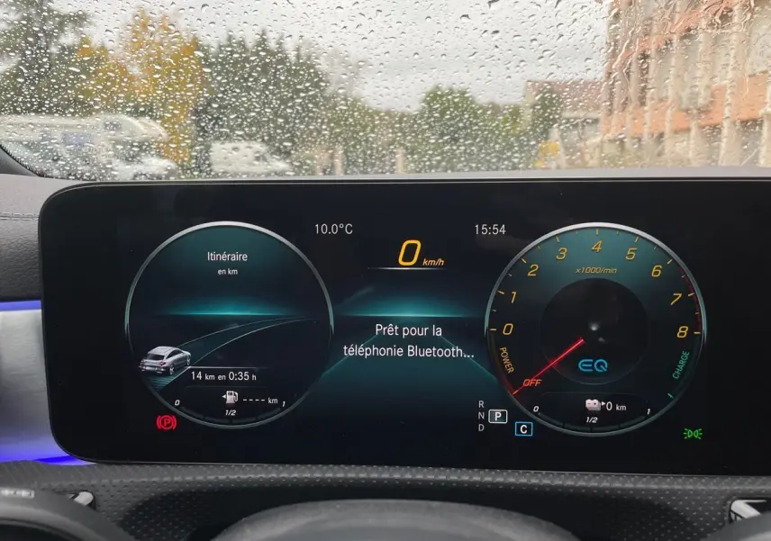 Tableau de bord numérique de Mercedes CLA Shooting Brake blanc, affichage du compteur et navigation sous la pluie.