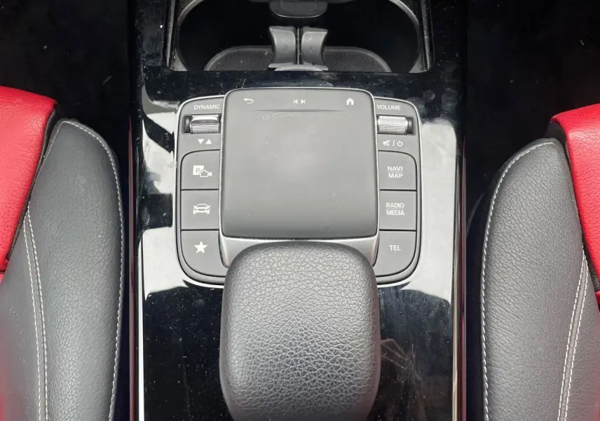 Gros plan sur la console centrale noire avec pavé tactile et pommeau de boîte automatique, sièges cuir rouge et noir visibles.