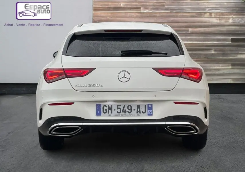 Vue arrière d'une Mercedes CLA Shooting Brake blanche avec feux allumés et double sortie d'échappement chromée.