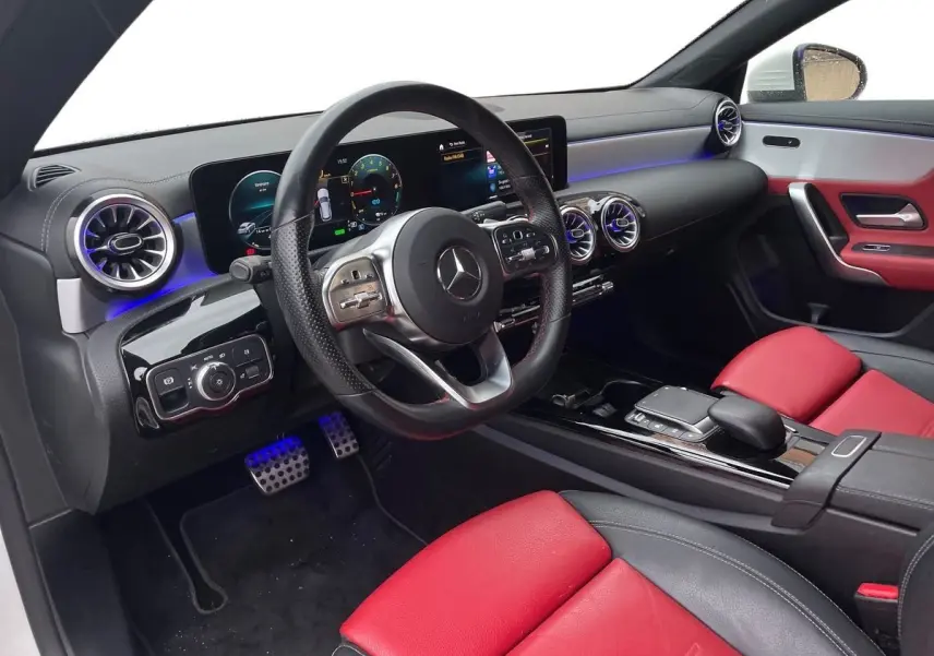 Intérieur côté conducteur de la Mercedes CLA Shooting Brake blanc, sièges cuir rouge et noir, tableau de bord digital AMG Line.