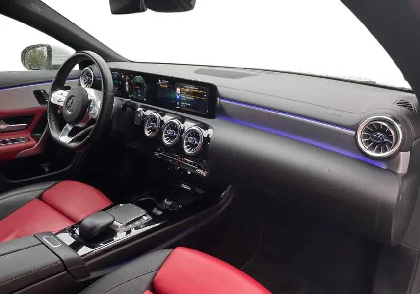 Vue intérieure côté passager de la Mercedes CLA Shooting Brake 250 E AMG Line 2021 avec sièges cuir rouge et éclairage d'ambiance bleu.