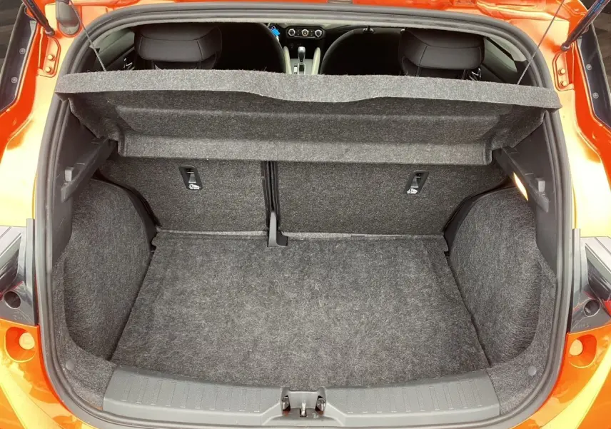 Vue arrière du coffre ouvert d'une Nissan Micra orange Energy 2022, montrant l'espace de chargement vide et la plage arrière relevée.