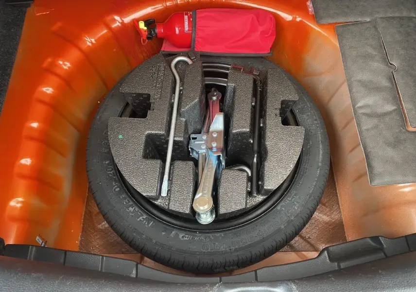 Vue plongeante sur la roue de secours et les outils dans le coffre orange energy d'une Nissan Micra 2022.