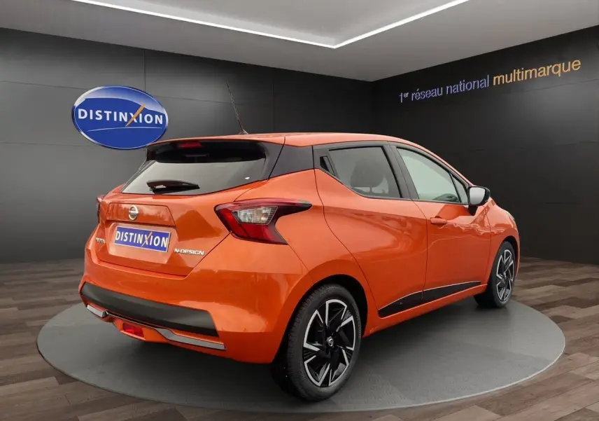 Vue 3/4 arrière droite d'une Nissan Micra 2022 orange Energy avec jantes noires et toit noir en showroom.