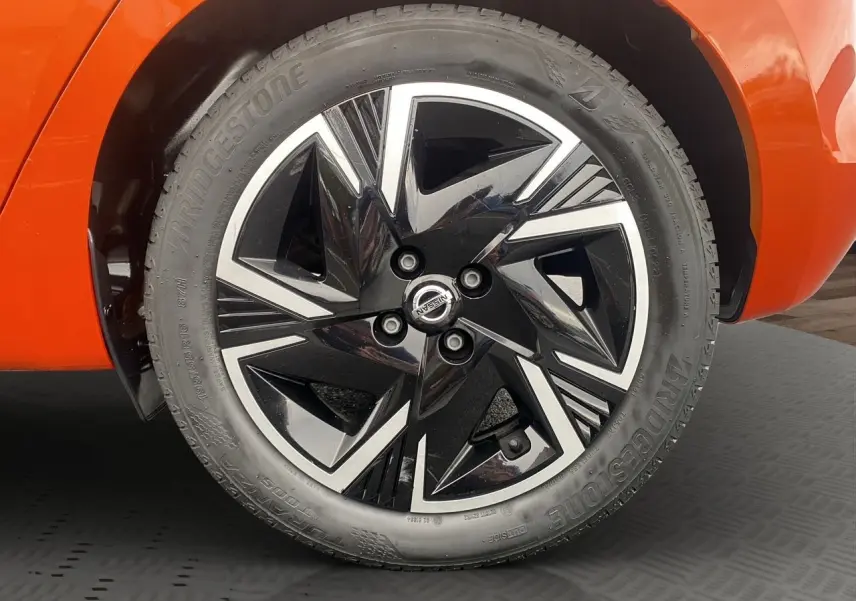 Gros plan sur la roue avant droite d’une Nissan Micra orange Energy, jante alliage noir et argent au design géométrique.