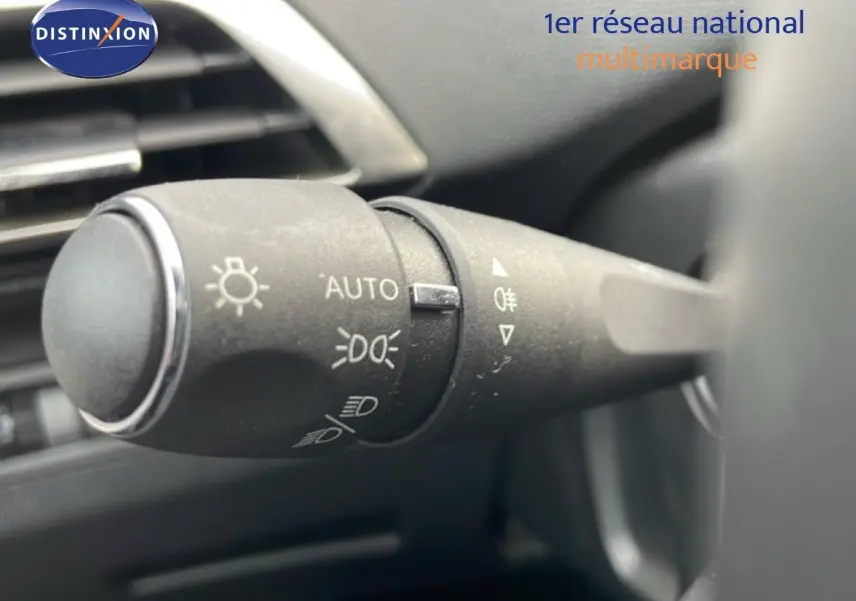 Gros plan sur la commande des phares du Peugeot 3008 hybride, bouton noir avec symboles lumineux, intérieur sombre.