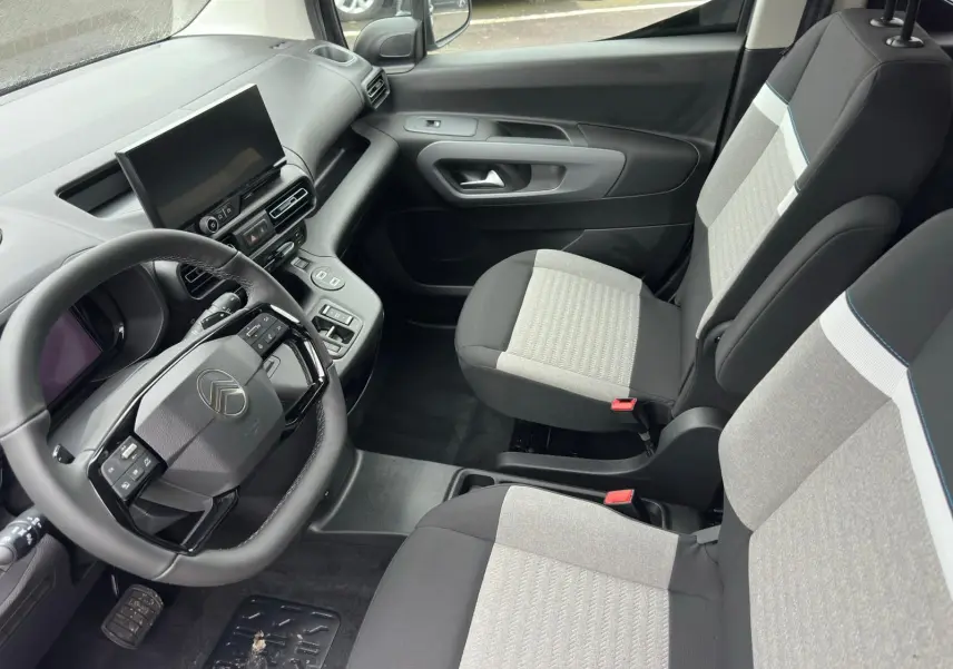 Vue intérieure côté conducteur du Citroën Berlingo 2025 avec sièges bicolores gris et noir et tableau de bord moderne.