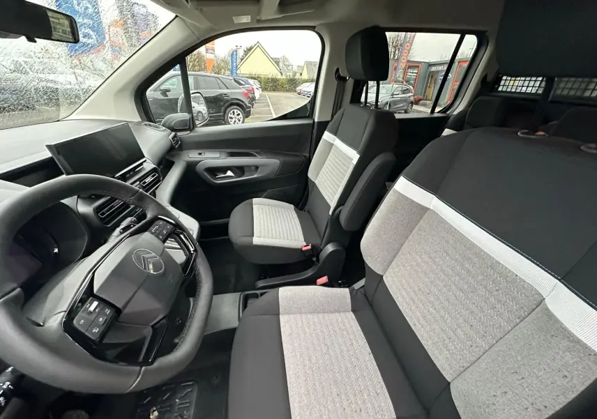 Vue intérieure côté conducteur du Citroën Berlingo 2025, montrant le volant, tableau de bord et sièges bicolores gris et noir.