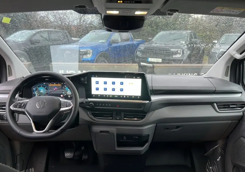 Vue intérieure frontale du tableau de bord gris clair du Volkswagen Transporter TDI 170 DSG avec écran tactile et volant multifonctions.