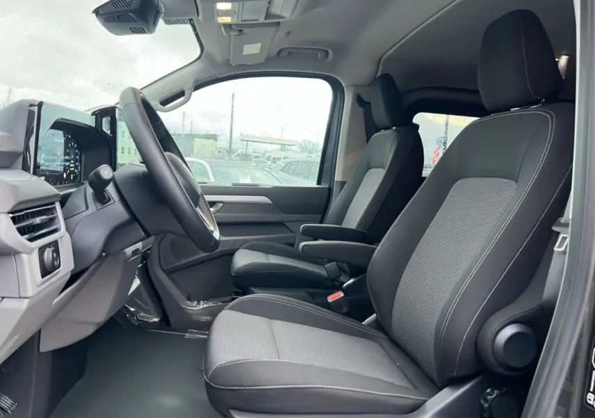 Vue intérieure côté conducteur du Volkswagen Transporter TDI 170 DSG Procab L2, sièges avant gris et noir avec accoudoirs.