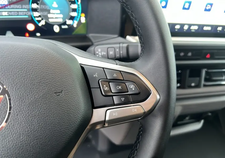 Gros plan sur le volant multifonctions noir du Volkswagen Transporter 2026 avec tableau de bord digital en arrière-plan.