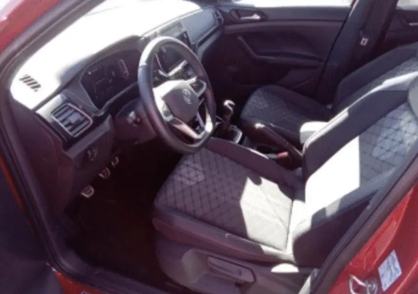 Vue intérieure côté conducteur du Volkswagen T-Cross rouge métal 2025, avec sièges en tissu et boîte manuelle.