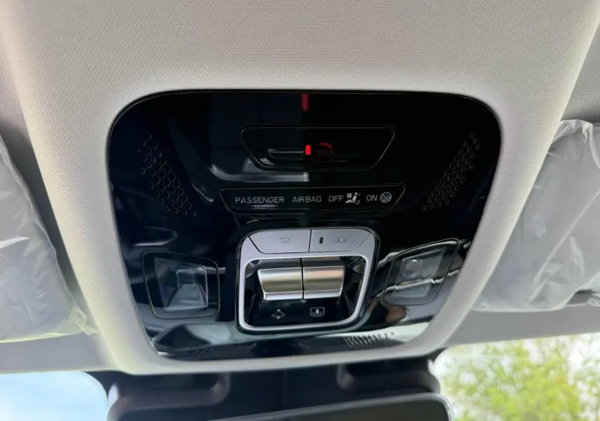 Vue intérieure en plongée sur la console de plafonnier noir brillant avec commandes d’éclairage et indicateur airbag passager du JAECOO J7 blanc.