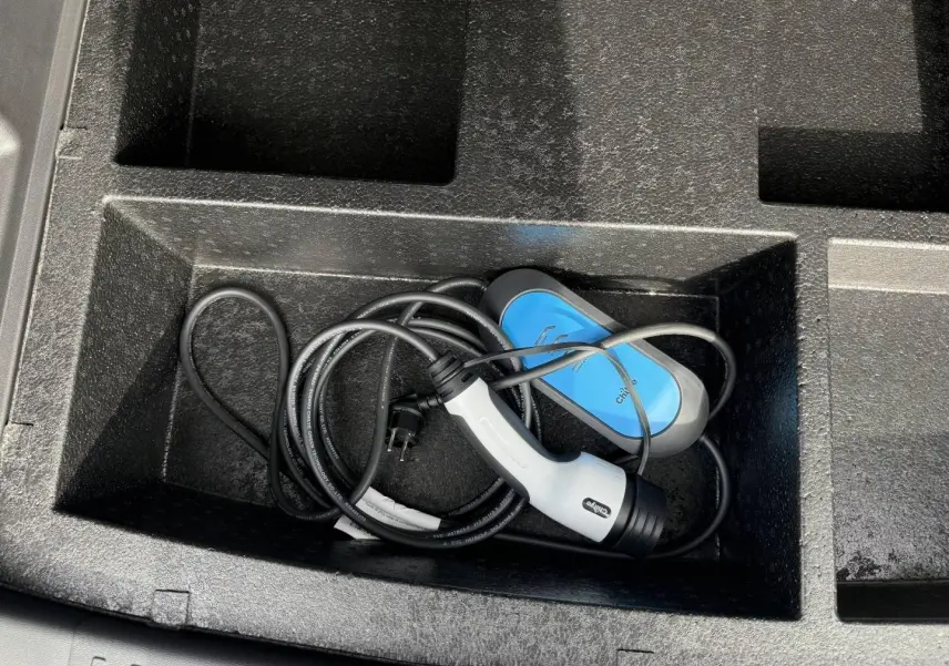 Gros plan sur le câble de recharge bleu et blanc rangé dans le coffre du JAECOO J7 hybride rechargeable blanc.