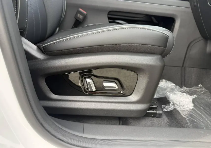 Gros plan sur les commandes électriques du siège conducteur noir dans un JAECOO J7 blanc, côté gauche.