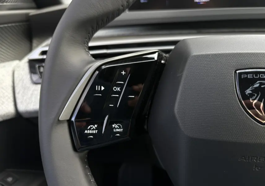 Gros plan sur le volant noir du Peugeot 5008 Hybrid 145 Allure 2025, avec commandes intégrées et logo lion central.