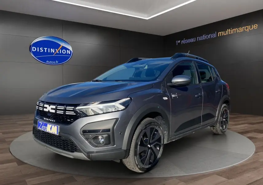 Vue 3/4 avant droite d'une Dacia Sandero Stepway gris schiste avec barres de toit et jantes noires.