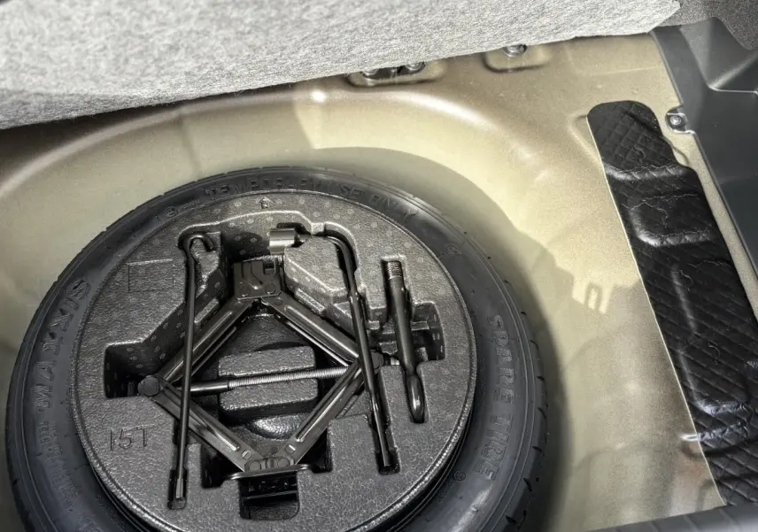 Vue rapprochée de la roue de secours et du cric dans le coffre d'une Hyundai i20 gris clair 2026.