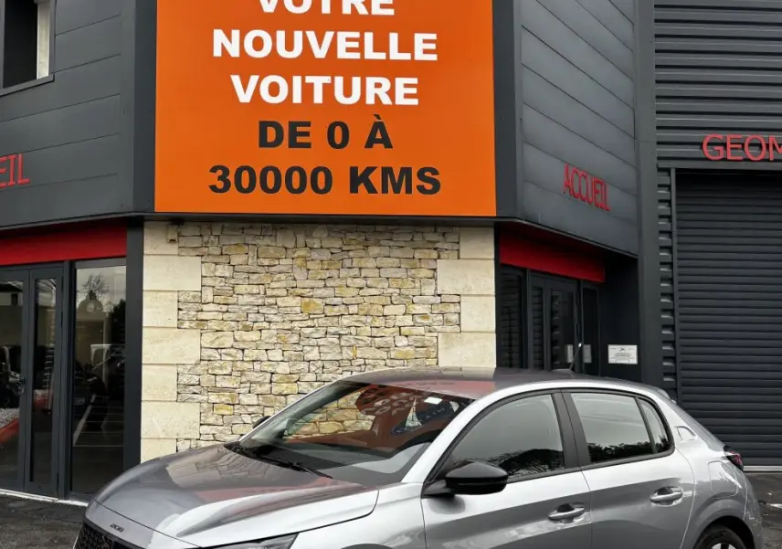 Peugeot 208 gris clair vue de profil droit devant un bâtiment avec panneau orange Distinxion.