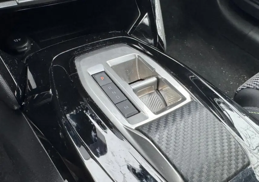 Gros plan sur la console centrale noire brillante de la Peugeot 208 Hybrid 110 e-DCS6 GT avec levier de boîte automatique.