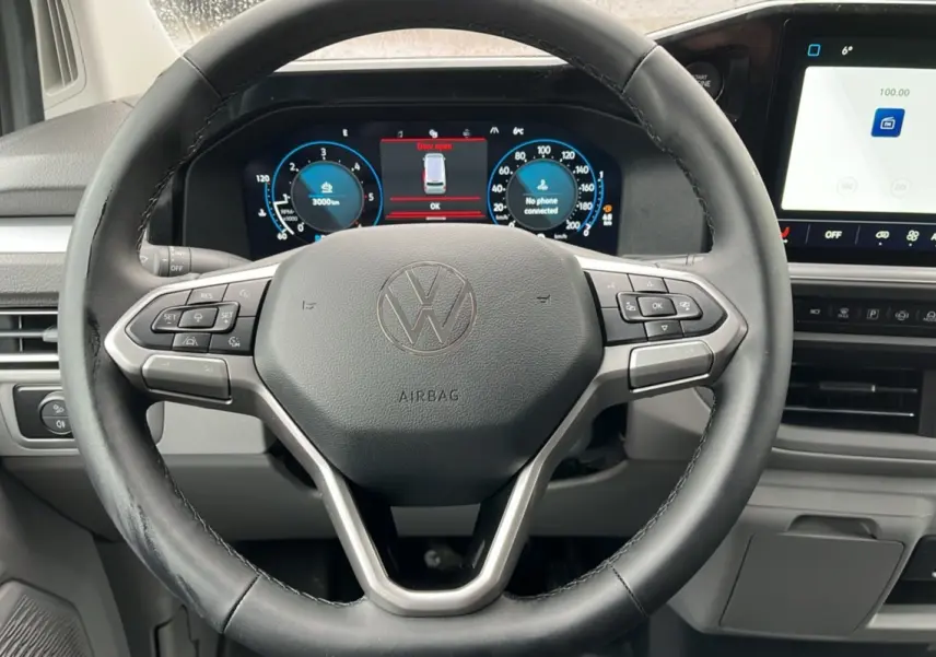 Vue rapprochée du volant multifonctions noir et du tableau de bord digital du Volkswagen Transporter TDI 170 DSG ProCab L2.