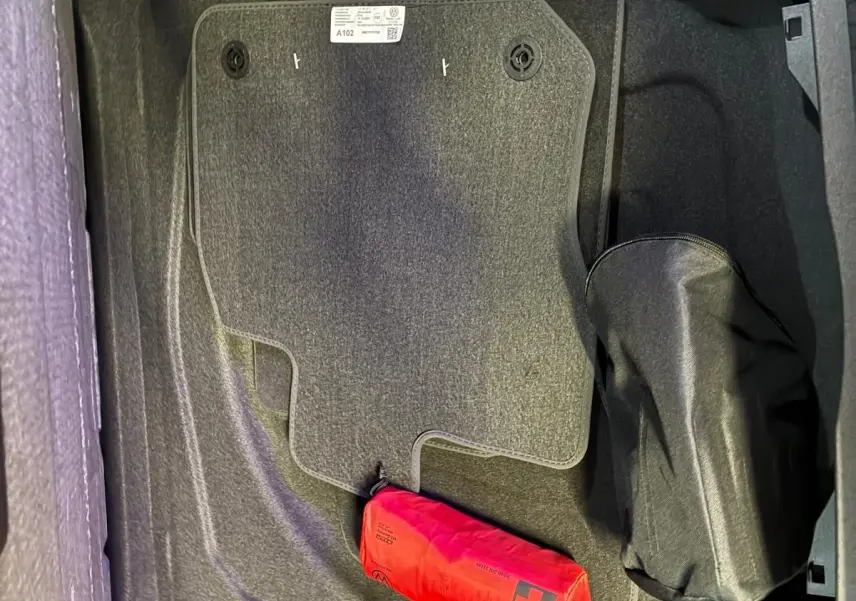 Coffre ouvert vu de dessus d’un Volkswagen Tiguan noir Grenadilla avec tapis de sol et trousse de secours rouge.
