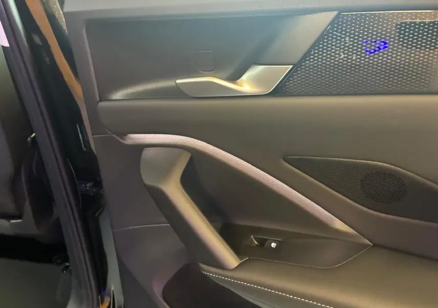 Gros plan sur la porte intérieure côté gauche du Volkswagen Tiguan noir avec poignée argentée et éclairage d’ambiance bleu.