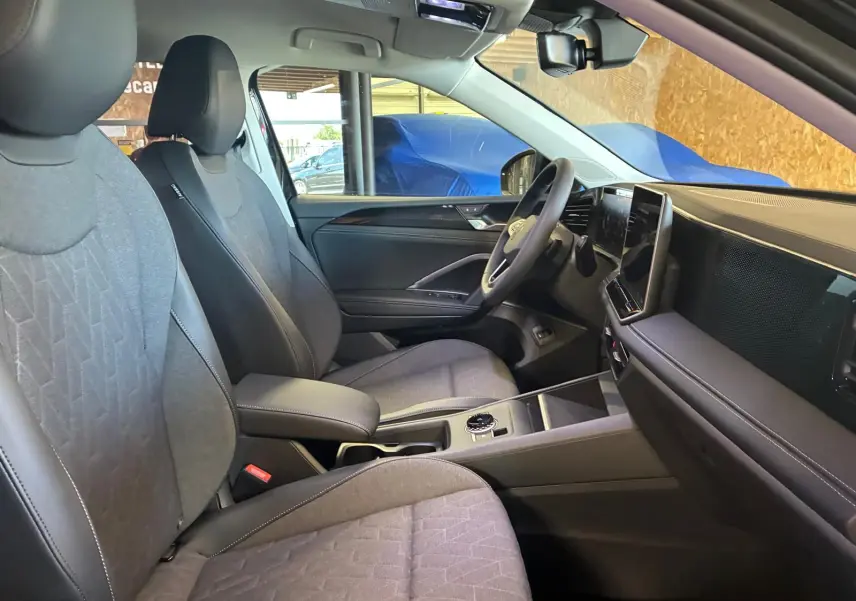 Vue intérieure côté conducteur du Volkswagen Tiguan 2026, sièges tissu gris et tableau de bord moderne avec écran tactile.