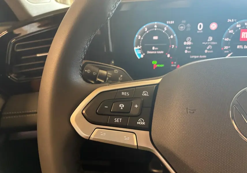 Gros plan sur le volant noir du Volkswagen Tiguan 2026, avec commandes de régulateur et tableau de bord digital en arrière-plan.