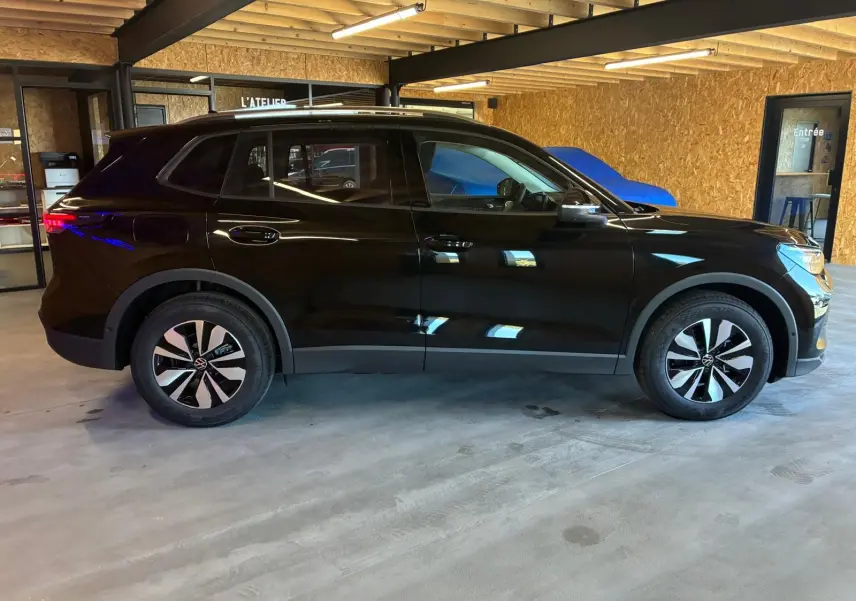 Vue de profil droit d'un Volkswagen Tiguan noir Grenadilla métallisé, avec jantes bi-ton et intérieur visible à travers les vitres.