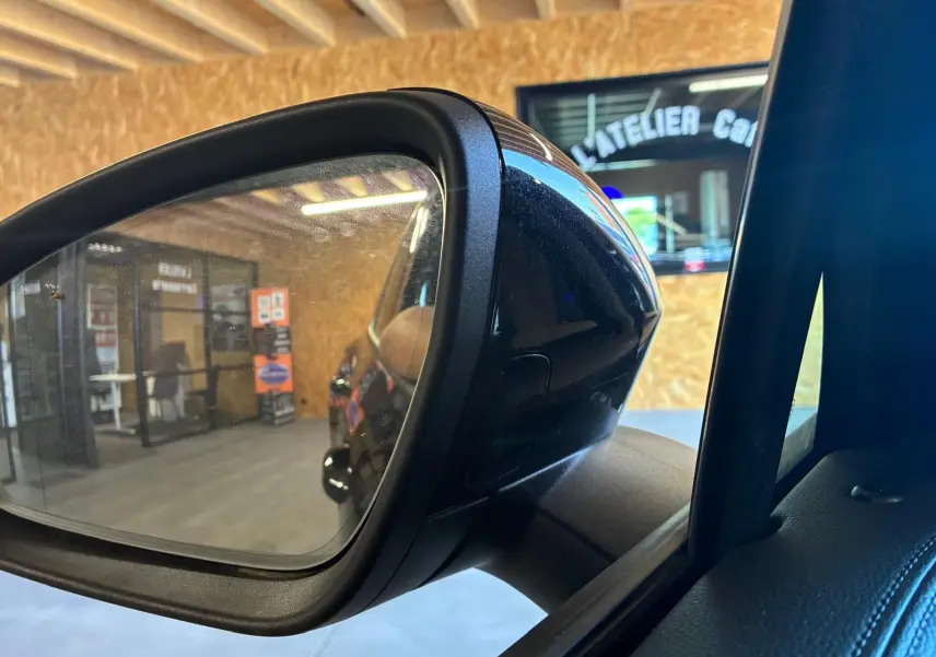 Rétroviseur extérieur côté gauche du Volkswagen Tiguan noir Grenadilla, reflet de l’intérieur d’un atelier.
