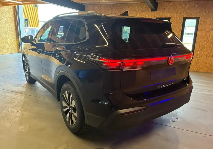 Vue 3/4 arrière droite du Volkswagen Tiguan noir Grenadilla avec feux arrière LED allumés en intérieur.
