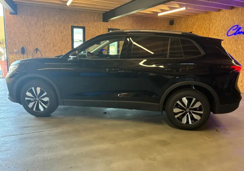 Volkswagen Tiguan 1.5 TSI noir grenadilla métal vu de profil côté gauche en intérieur avec jantes bicolores.