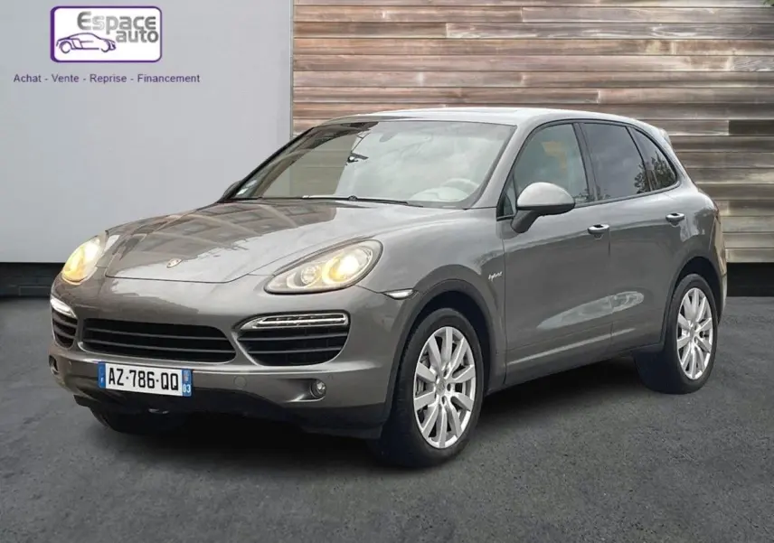 Porsche Cayenne S Hybrid gris vu en 3/4 avant droit avec phares allumés et jantes argentées.