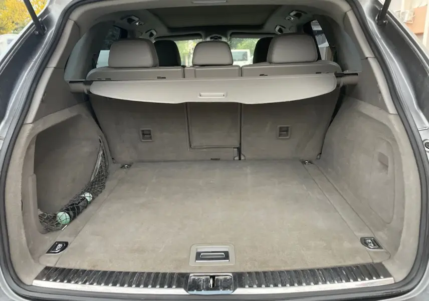 Coffre ouvert d'un Porsche Cayenne S Hybrid gris 2010, montrant un espace de chargement propre avec cache-bagages déployé.