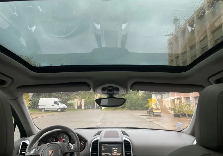 Vue intérieure du Porsche Cayenne S Hybrid 2010, montrant le tableau de bord, volant et toit panoramique sous la pluie.