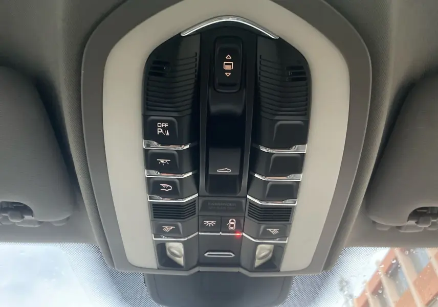 Vue en plongée sur le panneau de commandes au plafond du Porsche Cayenne S Hybrid gris de 2010, avec boutons lumineux.