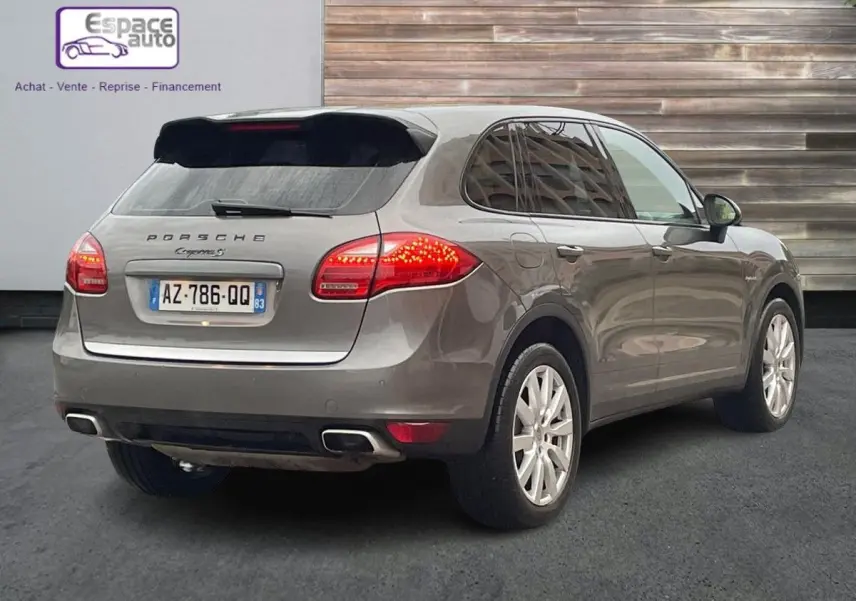 Vue 3/4 arrière droite d'un Porsche Cayenne S Hybrid gris 2010 avec feux arrière allumés et jantes argentées.