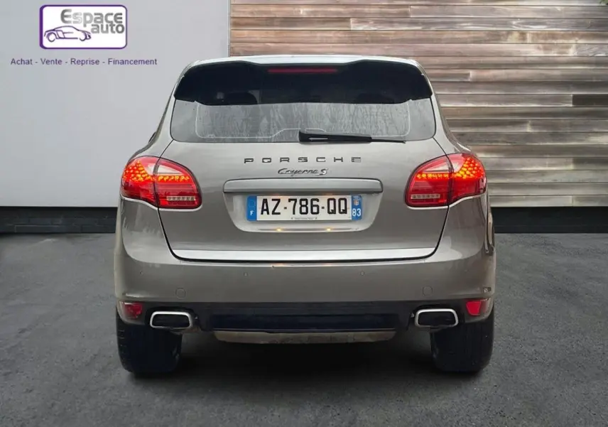 Vue arrière d'un Porsche Cayenne S Hybrid gris de 2010 avec feux allumés et double sortie d'échappement rectangulaire.