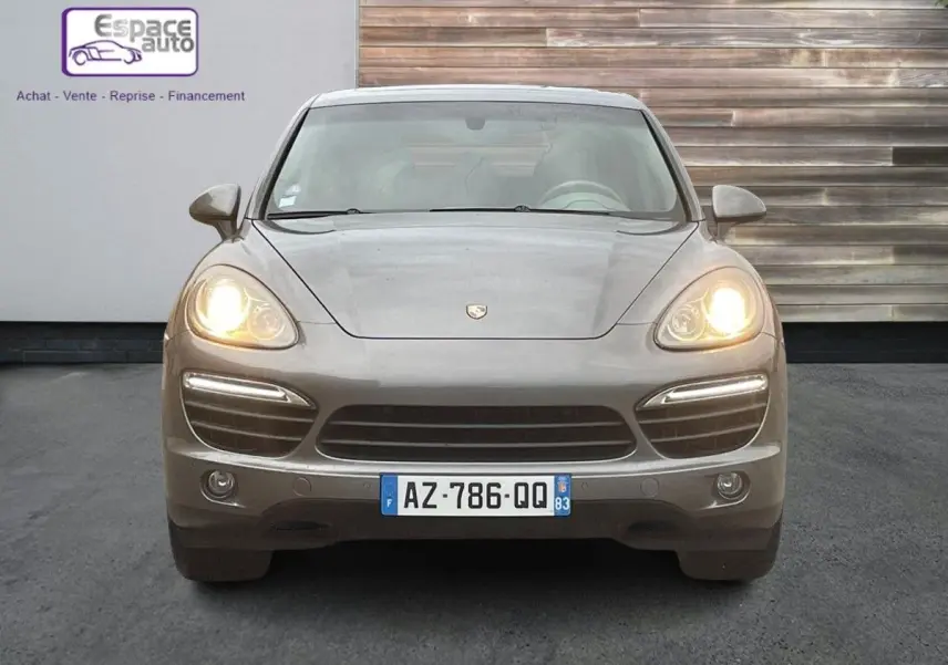 Vue frontale d'un Porsche Cayenne S Hybrid gris 2010 avec phares allumés et plaque d'immatriculation française visible.