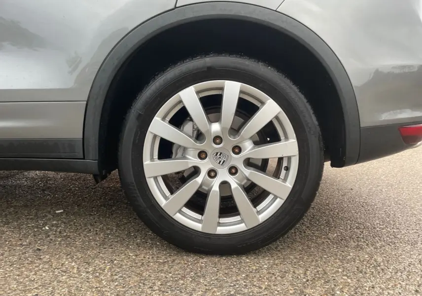 Gros plan sur la roue arrière droite d'un Porsche Cayenne S Hybrid gris 2010 avec jante alliage et logo Porsche central.